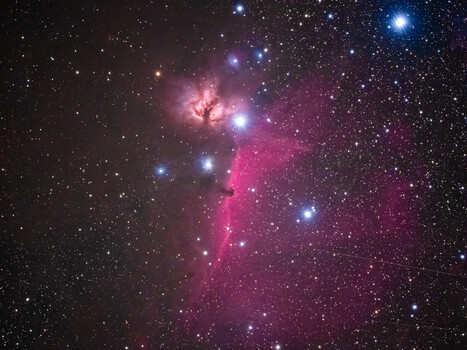 Deep space nebula with bright blue stars and pink emission clouds against starfield.