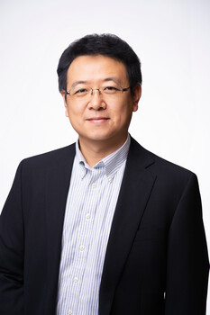 Professional headshot of an Asian man wearing glasses and a dark blazer over a light blue striped shirt.
