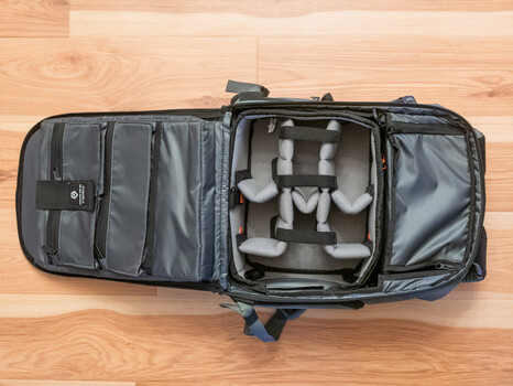 Open camera backpack with padded gray dividers holding a mirrorless camera and lenses on wooden floor.