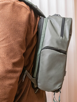 Person wearing a rust-colored ribbed shirt with a gray convertible backpack slung over one shoulder.