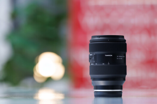 Tamron zoom lens positioned in sharp focus against a blurred background with warm and cool bokeh lights.