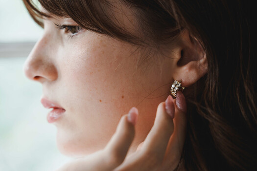 Woman in profile wearing ornate crystal stud earring, touching her ear with hand.