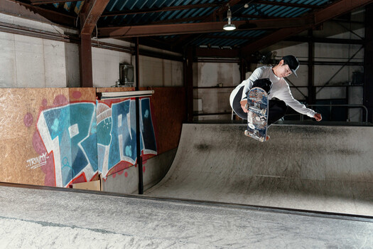 Skateboarder performing a trick on a concrete ramp in an indoor skate park.
