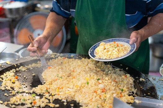 Street food vendor scooping fried rice from a large metal griddle onto a plate.