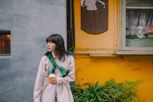 Woman in pink coat holding green vegetable against colorful urban building backdrop.