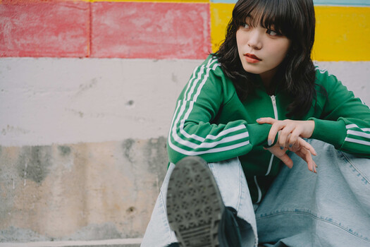 Woman in green striped track jacket posing against colorful geometric wall backdrop.