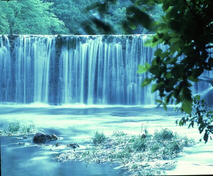 Cascading waterfall with turquoise water flowing over rocky ledges into a calm pool below.