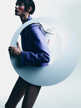 Man in blue jacket holding a large white sphere against a neutral background.
