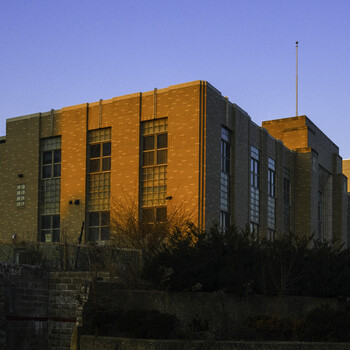 Golden-hour sunlight illuminates a modernist brick building with geometric window patterns and a radio antenna.
