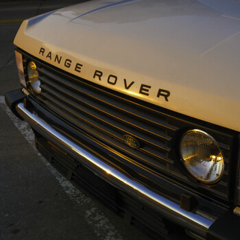Close-up of a yellow Range Rover's front grille and headlight, photographed in natural daylight.