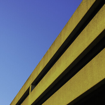 Yellow concrete overpass with dark shadow lines against clear blue sky.