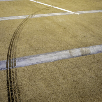 Tire tracks curve across a sandy surface marked by white boundary lines.
