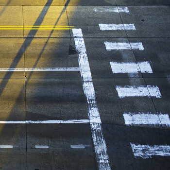 Overhead view of pavement markings with yellow and white lines creating geometric patterns and shadows.