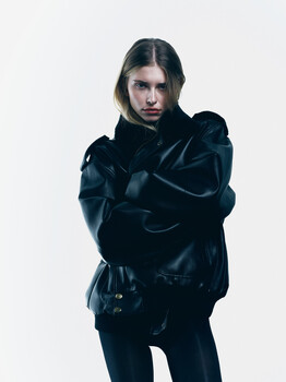 Woman in dark clothing with arms crossed against neutral background.