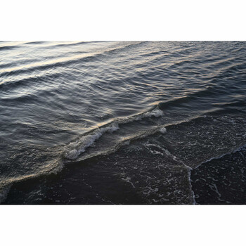 Ocean waves rolling onto a dark sand beach during golden hour, with layered water reflections and foam patterns.