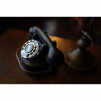 Two vintage rotary dial telephones with black Bakelite handsets arranged on a wooden surface under warm lighting.