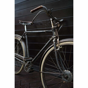 Vintage steel-frame bicycle with drop handlebars and curved fenders, photographed against dark wooden wall paneling.