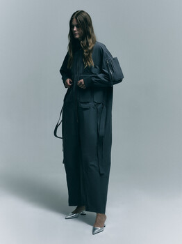 Woman in dark oversized blazer and trousers posed against neutral gray backdrop.