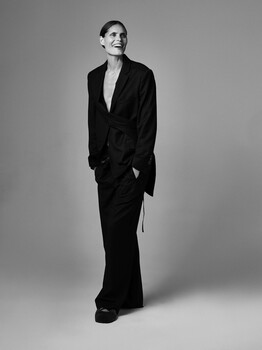 Person in black oversized blazer and trousers standing against neutral background.