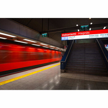 Red subway train departing station platform with yellow safety line and stairs visible.