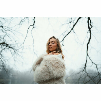 Woman in cream-colored fuzzy sweater standing against bare winter branches and overcast sky.