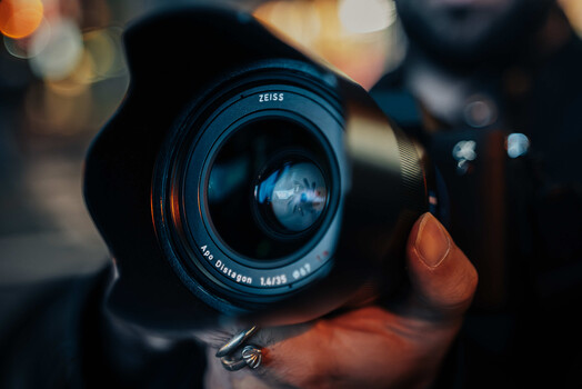 Zeiss camera lens held in hand with warm and cool bokeh lighting in background.