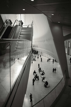 Elevated view of a modern transit station floor with scattered pedestrians and escalators visible in the upper frame.