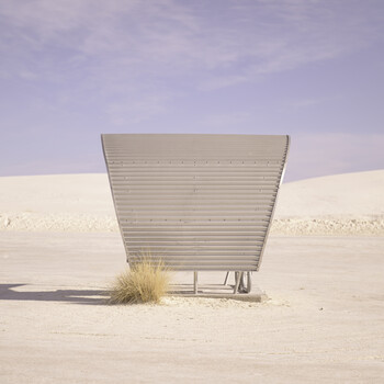 Corrugated metal structure abandoned in vast desert landscape with sparse vegetation and purple sky.