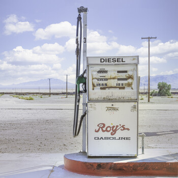 Abandoned vintage diesel fuel pump under bright daylight with scattered clouds and mountains in the distance.
