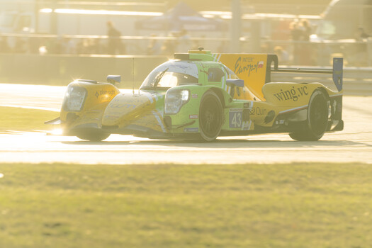 Green and yellow race car with aerodynamic bodywork on a sunny race track.