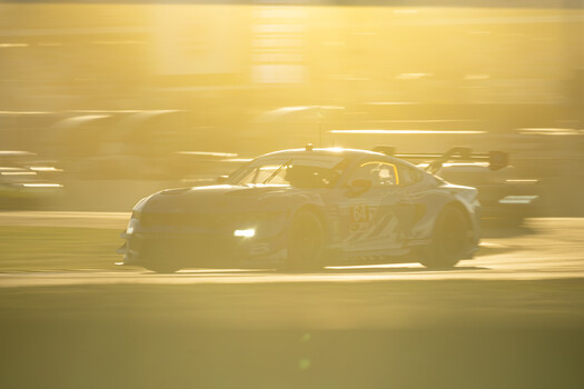 Sports car captured with motion blur on a race track during golden hour lighting.