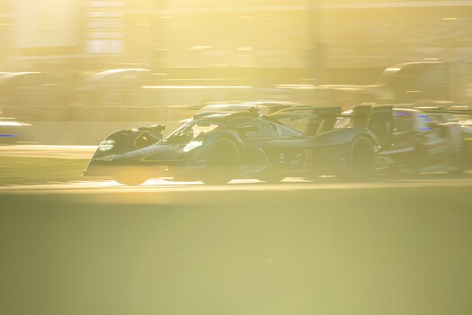 Dark sports car captured with motion blur on a racetrack during golden hour.