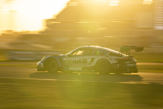 White racing car with aerodynamic body kit captured mid-motion with motion blur effect during golden hour.
