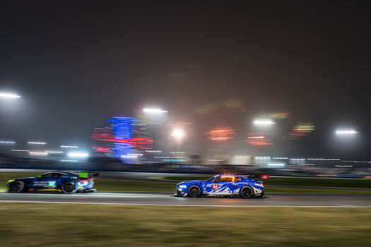 Two blue race cars competing on an illuminated nighttime race track with motion blur.