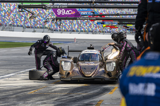 Pit crew members service a racing prototype during a pit stop at a professional motorsports event.