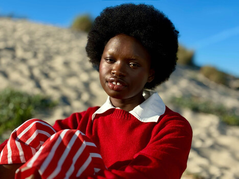 Woman in red sweater with white collar posed against rocky hillside under clear sky.