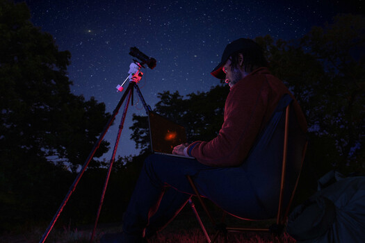 Astronomer observing the night sky through a telescope mounted on a tripod under a starry sky.