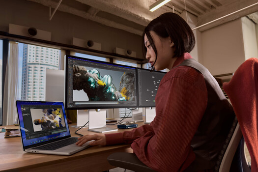 Video editor working at a desk with dual monitors displaying color-graded footage in editing software.