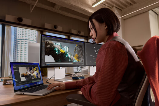 Video editor working on color grading at a desk with dual monitors displaying edited footage.