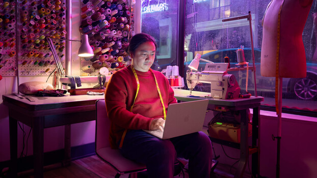 Person working on laptop in neon-lit studio workspace with purple and pink ambient lighting.