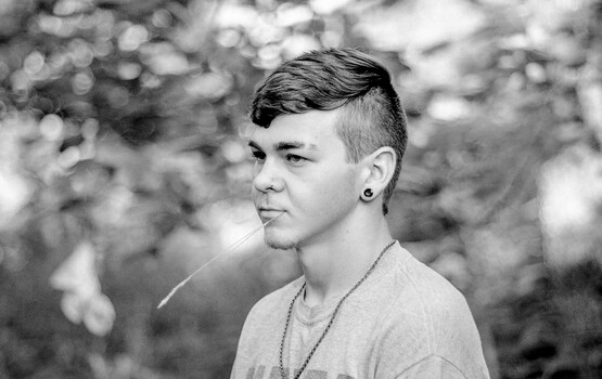 Young man in profile wearing a light-colored t-shirt and chain necklace, photographed in black and white.