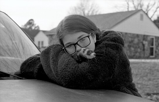 Person wearing glasses resting on car hood in black and white portrait.