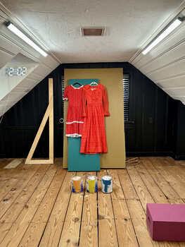 Red clothing displayed on wooden panel in minimalist studio space with angled ceiling and fluorescent lighting.