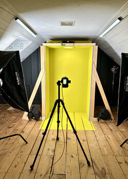 Studio setup with camera on tripod positioned in front of bright yellow backdrop and softbox lighting.