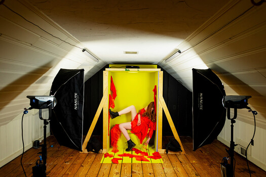 Studio setup with red peppers on yellow surface, flanked by softboxes and key lights in an attic space.