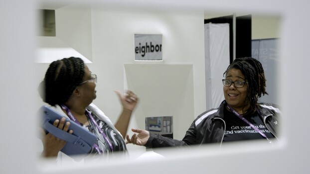 Two women having a conversation in an indoor space with signage visible in the background.