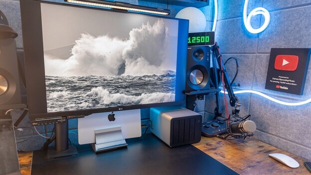 Content creator workspace with monitor displaying ocean wave photograph, professional lighting setup, and neon YouTube branding.