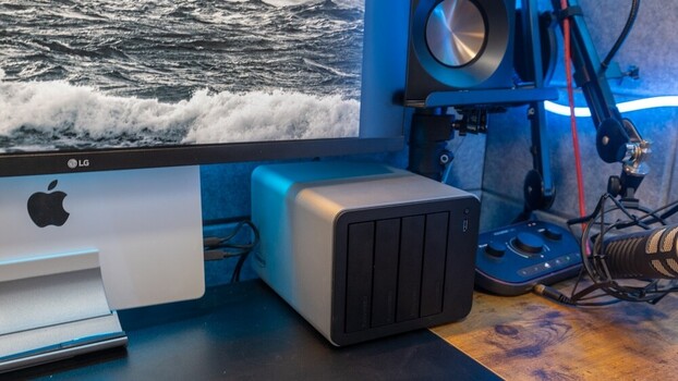 Creative workspace with Mac monitor, external storage device, studio lighting, and 3D printer against ocean backdrop.