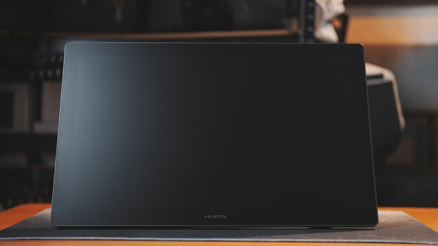 Portable display monitor with dark screen sitting on orange surface in studio setting.