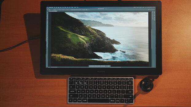 Photo editing workspace showing a coastal landscape with green cliffs displayed on a monitor with keyboard and stylus.